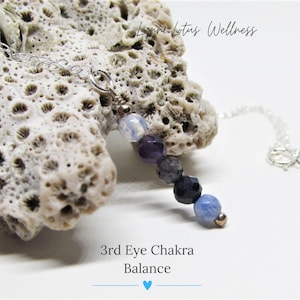 May include: A silver chain necklace with a pendant made of blue, purple, and white gemstone beads. The pendant is labeled "3rd Eye Chakra Balance".