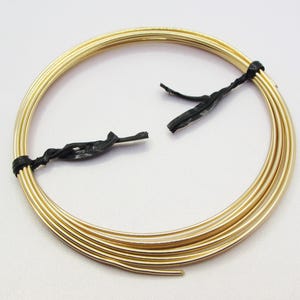 May include: A coiled length of metallic gold-colored craft wire arranged in a circular shape. The wire is secured in two places by thin black plastic ties that hold the multiple loops of the coil together in a uniform, rounded configuration.
