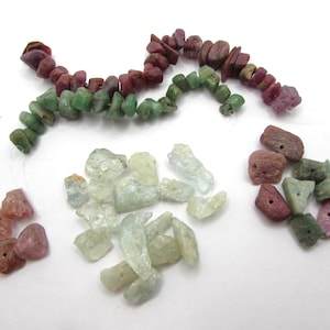 May include: Assortment of gemstone beads in various shades of pink, green, and light blue. The beads are irregular in shape and have a rough, natural texture.