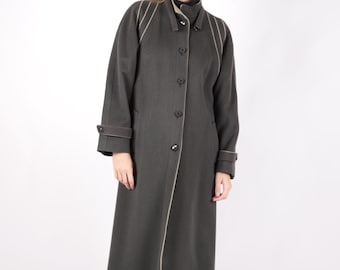 May include: A long, dark green coat with a button-up front and a tailored fit. The coat features light brown trim along the edges and cuffs. The model is wearing black boots.
