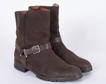 May include: A pair of brown leather ankle boots with a buckle strap detail. The boots have a low heel and a rounded toe.