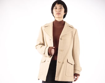 Puede incluir: Un abrigo de lana beige con un jersey de cuello alto marrón debajo. El abrigo tiene cierre de botones, dos bolsillos de solapa y un solo botón en cada puño.