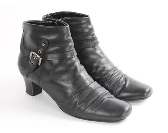 May include: A pair of black leather ankle boots with a buckle detail on one boot. The boots have a low block heel and a square toe.