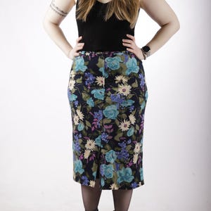 May include: A floral midi skirt with a dark blue background and a variety of blue, purple, and yellow flowers. The skirt has a front slit and is worn with black tights and black ankle boots.