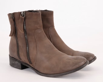 May include: A pair of brown leather ankle boots with two zippers on each side. The boots have a low heel and a rounded toe.