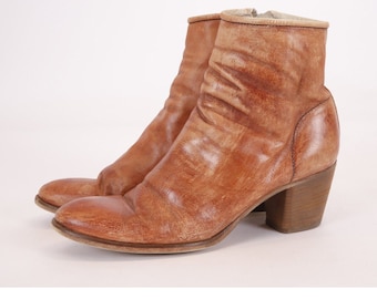 May include: Brown leather ankle boots with a block heel. The boots have a distressed look and a pointed toe.