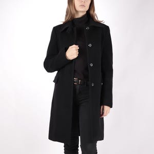 May include: A black long-sleeved coat with a high collar and button closure. The coat has a simple design and is made of a smooth fabric.