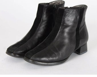 May include: Black leather ankle boots with a suede panel on the side. The boots have a low block heel and a zipper closure on the inside.