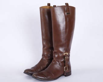 May include: A pair of brown leather riding boots with gold buckles. The boots have a pointed toe and a low heel.