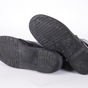 May include: A pair of black leather boots with a thick rubber sole. The boots are shown from the bottom, with the soles facing the camera.