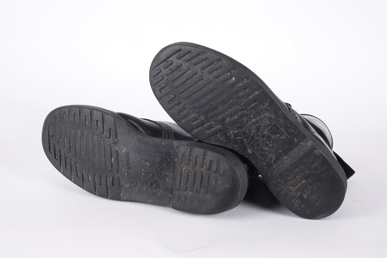 May include: A pair of black leather boots with a thick rubber sole. The boots are shown from the bottom, with the soles facing the camera.