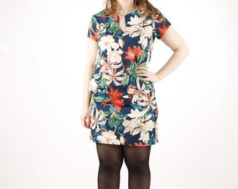 Puede incluir: Una mujer lleva un vestido corto de manga corta, de color azul marino con estampado floral. El vestido tiene cuello en V y un corte holgado. Lleva medias negras y botines de color marrón claro.