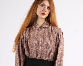 May include: A long-sleeved paisley patterned blouse with a collared neckline. The blouse is in shades of brown, beige, and red.