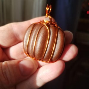 May include: A brown pumpkin-shaped pendant wrapped in copper wire. The pendant has a shiny, metallic finish.