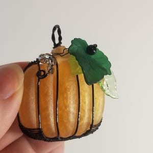 May include: A small orange glass pumpkin with a black wire frame and green leaves. The pumpkin has a black bead on the top of the leaf.
