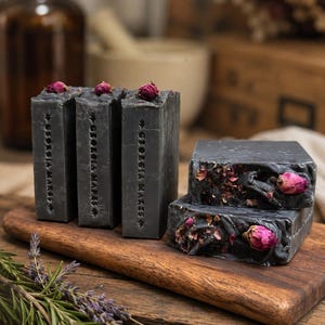 May include: Three rectangular charcoal-colored soap bars standing upright and two stacked horizontally, all featuring the embossed text "GEORGIA MAKES" and small dried pink rosebuds embedded on the top and side surfaces.