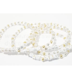 May include: A set of six beaded bracelets with gold and silver beads. Each bracelet has a different word spelled out in white letters: "Boss", "Babe", "Faith", "Worry", "Grateful", and "Bless".