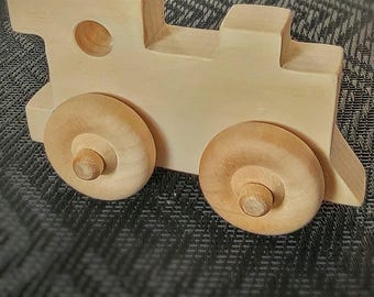 May include: A wooden toy train with two large wheels and a small smokestack. The train is made of light-colored wood and has a simple, classic design. The wheels are round and attached to the body with wooden pegs.