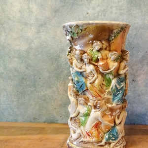 May include: A ceramic vase with a detailed relief design of multiple figures in various colors, including blue, green, yellow, and orange. The vase has a distressed, aged look.