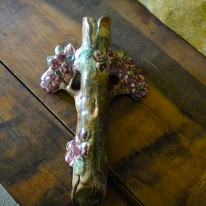 May include: A ceramic vase shaped like a tree trunk with brown and green glaze. The vase is decorated with pink and red flowers.