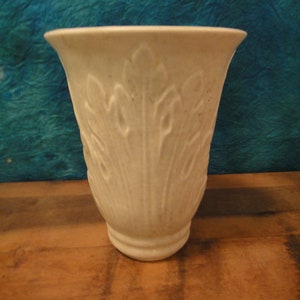 May include: White ceramic vase with a raised leaf design. The vase has a wide mouth and a narrow base.