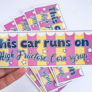 May include: A set of six pink and yellow striped car bumper stickers with the text "This car runs on High Fructose Corn Syrup" and a star design.