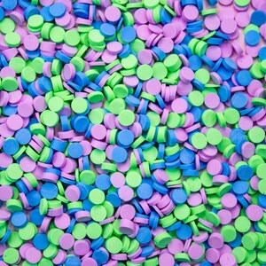 May include: A close-up image of a large quantity of small, round sprinkles in three colors: light blue, light green, and light purple. The sprinkles are scattered randomly across the surface.
