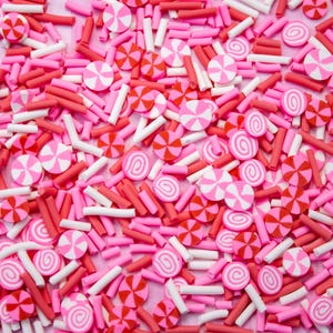 May include: A close-up of pink and white candy sprinkles. The sprinkles are in the shape of candy canes and swirls.