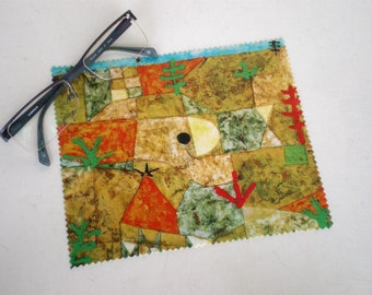 May include: A colorful abstract art print on a microfiber cleaning cloth. The print features geometric shapes in shades of red, orange, yellow, green, and brown. A black circle is in the center of the print.