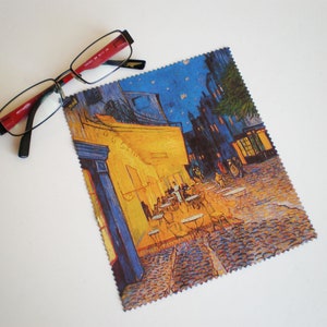 May include: A microfiber cleaning cloth with a printed image of Vincent van Gogh's "The Starry Night Over the Rhone" painting. The painting depicts a cafe at night with a starry sky and a yellow building.