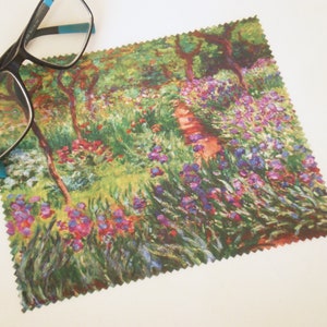 Op de afbeelding: Een microvezel schoonmaakdoek met een kleurrijk schilderij van een tuinscene. Het schilderij toont een verscheidenheid aan bloemen, bomen en bladeren in tinten groen, paars, roze en geel.