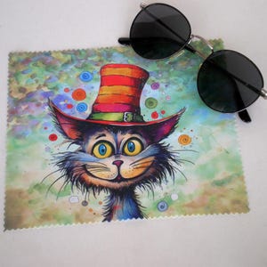 May include: A colourful microfiber cleaning cloth featuring a cartoon cat wearing a red, yellow and green striped hat. The cat has blue eyes and a big smile. The background is a watercolour wash of green, blue and yellow.