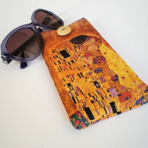 Könnte beinhalten: Ein gelbes, braunes und blaues Brillenetui aus Stoff mit einem Druck von Gustav Klimts Gemälde Der Kuss. Das Etui hat einen Knopfverschluss.