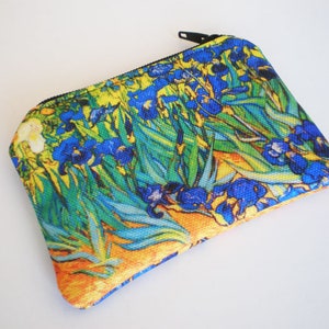 May include: A small, rectangular zippered pouch featuring a print of Vincent van Gogh's "Irises" painting. The pouch displays vibrant blue irises, green foliage, and yellow and orange accents against a light background. The zipper is black.