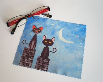 May include: A blue microfiber cleaning cloth with a crescent moon and stars design. Two black cats with white eyes are perched on brick chimneys.