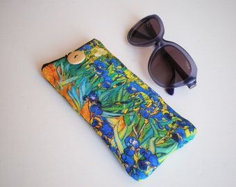 May include: A blue and yellow floral print glasses case with a wooden button closure. The case is lying on a white surface next to a pair of purple sunglasses.