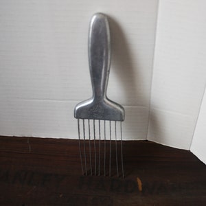 May include: A silver metal comb with a long handle and a row of tines. The comb is labeled "Regina 700".
