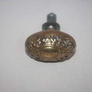 May include: A gold-toned oval door knob with intricate floral designs. The knob has a silver-toned screw.
