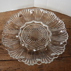 May include: A clear glass serving dish with a scalloped edge and a center section with a starburst pattern. The dish is perfect for serving snacks, appetizers, or desserts.