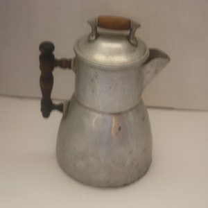 May include: A silver aluminum coffee pot with a wooden handle. The pot has a rounded body and a spout on the side.