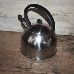 May include: A silver stainless steel kettle with a black plastic handle and lid. The kettle has a rounded body and a spout on the side.