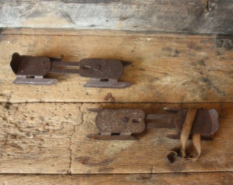 May include: Two rusty metal ice skate blades with leather straps. The blades are attached to a wooden surface.