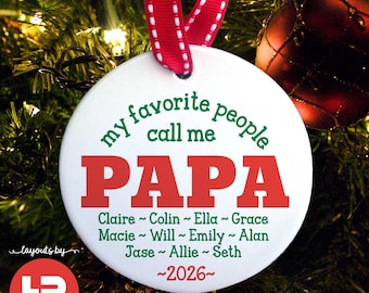 May include: White round Christmas ornament with red and green text that reads "my favorite people call me PAPA". Includes names and the year "2026". The ornament hangs from a red and white ribbon.