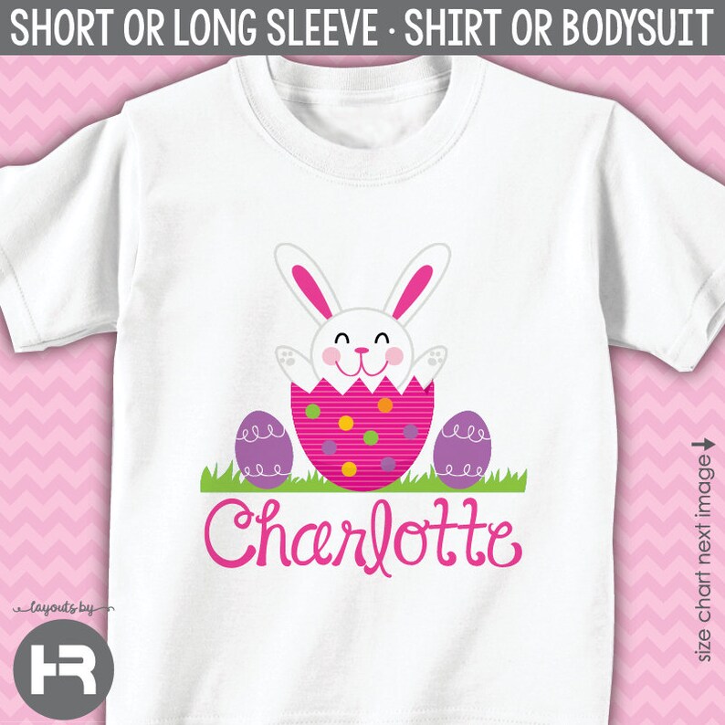 May include: White t-shirt with a pink Easter bunny peeking out of an egg with purple and pink polka dots. The bunny has a pink nose and pink ears. The text "Charlotte" is written in pink below the bunny.