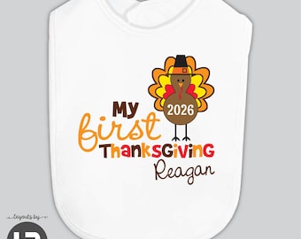May include: A white baby bib featuring a graphic of a brown turkey wearing a black hat. The text reads My first Thanksgiving 2026 Reagan. The turkey has orange and yellow feathers, and the lettering uses brown, orange, and red colors.