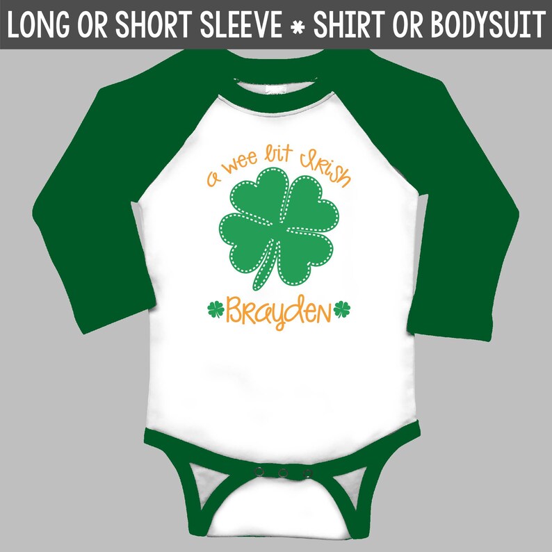Pu&ograve; includere: Una maglietta o un body bianco a maniche lunghe o corte con maniche raglan verdi. La maglietta presenta un trifoglio a quattro foglie verde con cuciture arancioni e il testo "a wee bit Irish" in arancione. Il nome "Brayden" &egrave; scritto in arancione sotto il trifoglio.