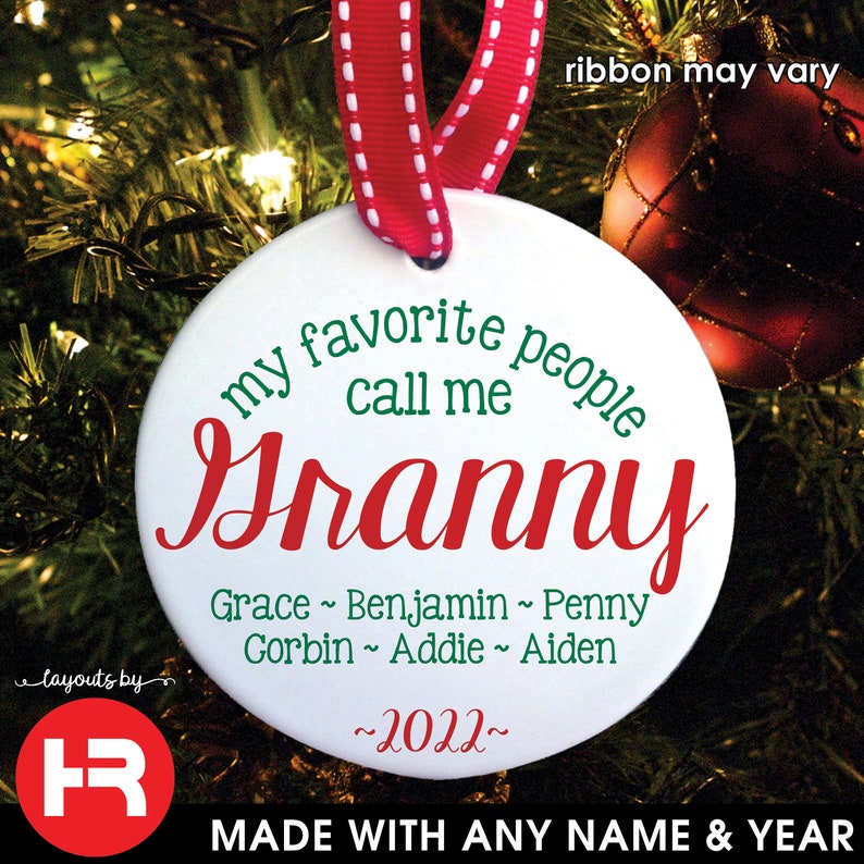 May include: A white ceramic Christmas ornament with a red and white ribbon. The ornament has the text "my favorite people call me Granny" in green and red. Below the text are names and the year 2022.