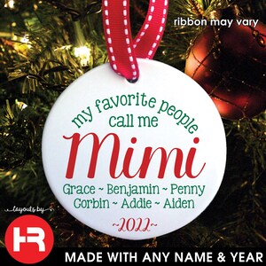May include: A white, round Christmas ornament with the text "my favorite people call me Mimi" in green and red. Below, names and the year 2022 are listed. It hangs from a red ribbon with white stitching, against a blurred Christmas tree background.
