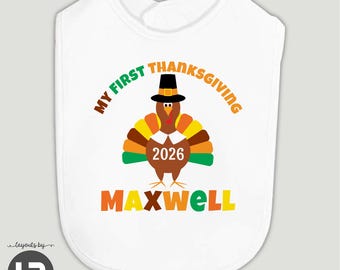May include: A white baby bib featuring a brown turkey wearing a black pilgrim hat and a white collar. The text reads MY FIRST THANKSGIVING, 2026, and MAXWELL in orange, green, and yellow lettering centered on the front of the fabric.
