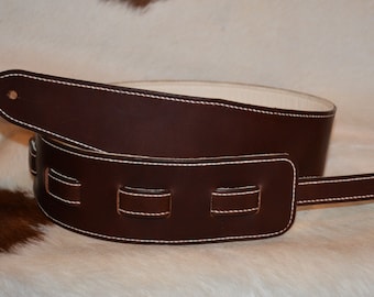 May include: A brown leather guitar strap with white stitching and a decorative design. The strap has a buckle and a strap adjuster.